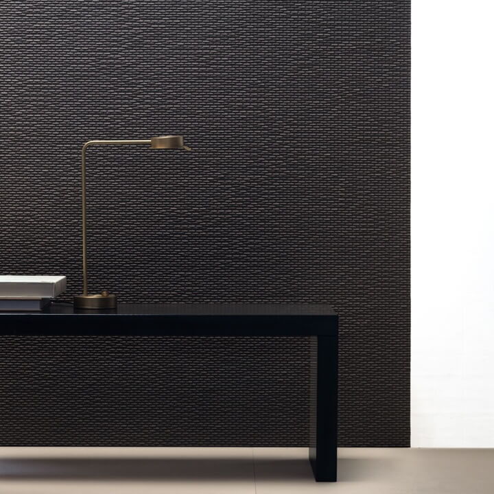 schwarze mit länglicher Struktur versehene Wandfliesen, davor ein schwarzes Regal mit goldener Stehlampe
