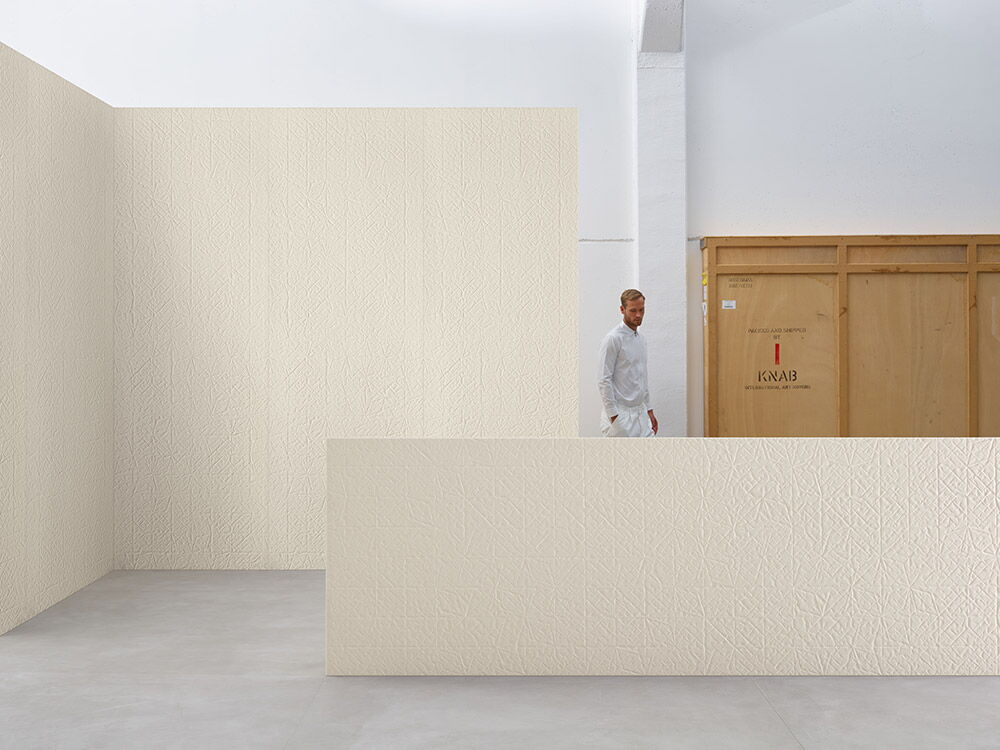 sehr große Designerfliesen Folded XL; dahinter steht ein Mann, der erst ab der Hüfte zu sehen ist; im Hintergrund eine Wand mit der gleichen Fliese