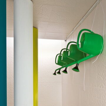 Wand und Decke mit der weißen, strukturierten Designerfliese Folded; von der Decke hängen grüne Gießkannen hinab
