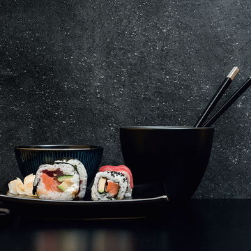 schwarz verputzte, strukturierte Wand mit dunklen Sushi-Teller und Schüsseln davor