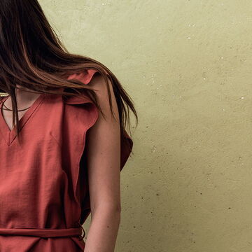 grün-grau verputzte Wand mit Struktur, davor angeschnitten eine Frau im roten Leinenkleid