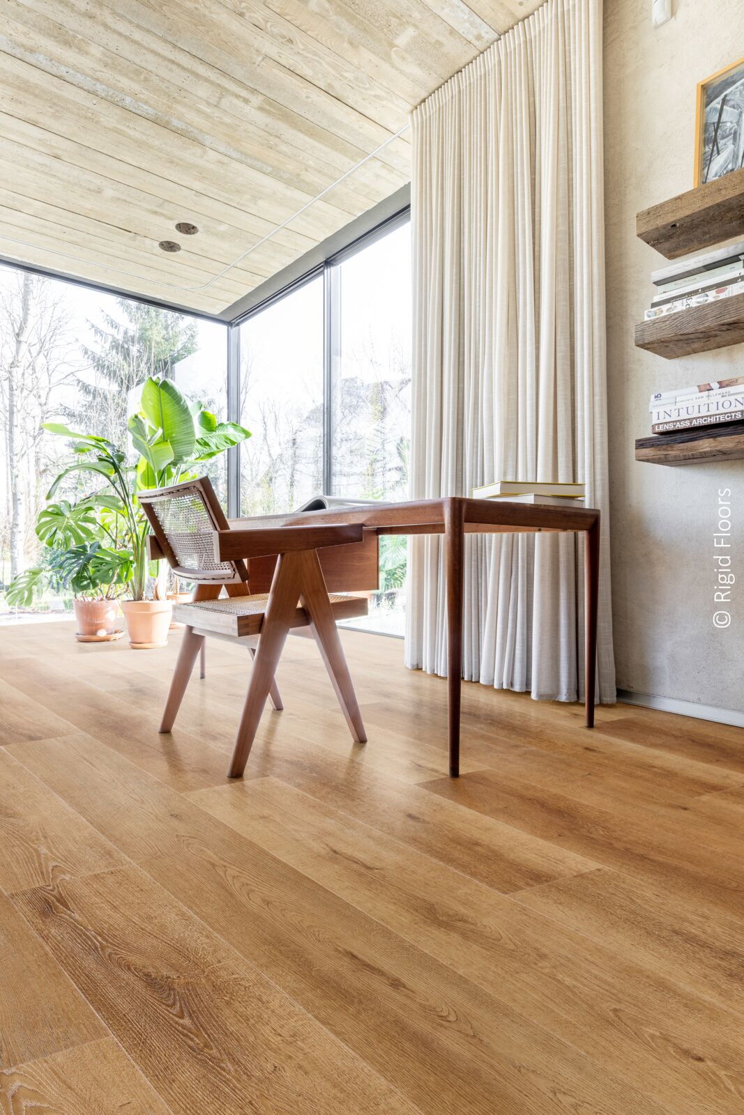 Wohnraum mit großer Fensterfront und Holzschreibtisch und -stuhl auf braunem SPC-Fußboden in Holzoptik