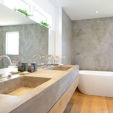 modernes, großes, helles Bad mit grauer Wand, freistehender Badewanne und zwei Waschbecken in Beton-Optik