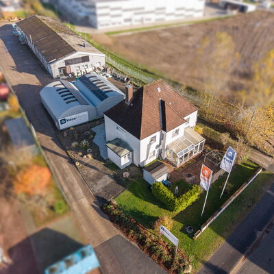 Blick von oben auf ein weißes Haus mit Wintergarten, dahinter mehrere Lagergebäude